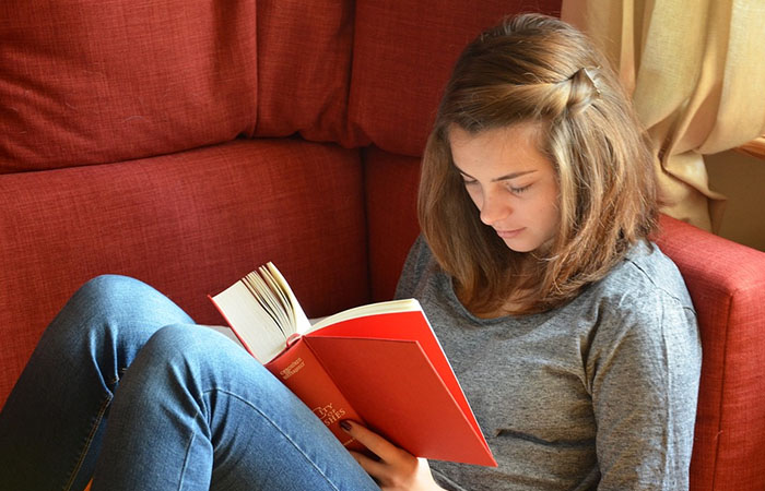 Kvindelig studerende læser en rød bog i rød stol
