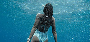 Kvinde under vand svømmer op mod havoverfladen